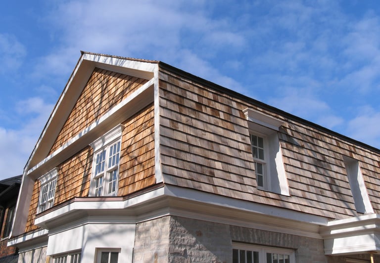 Two-story house with wooden shake shingle siding, white trim, and gabled roof against a blue sky